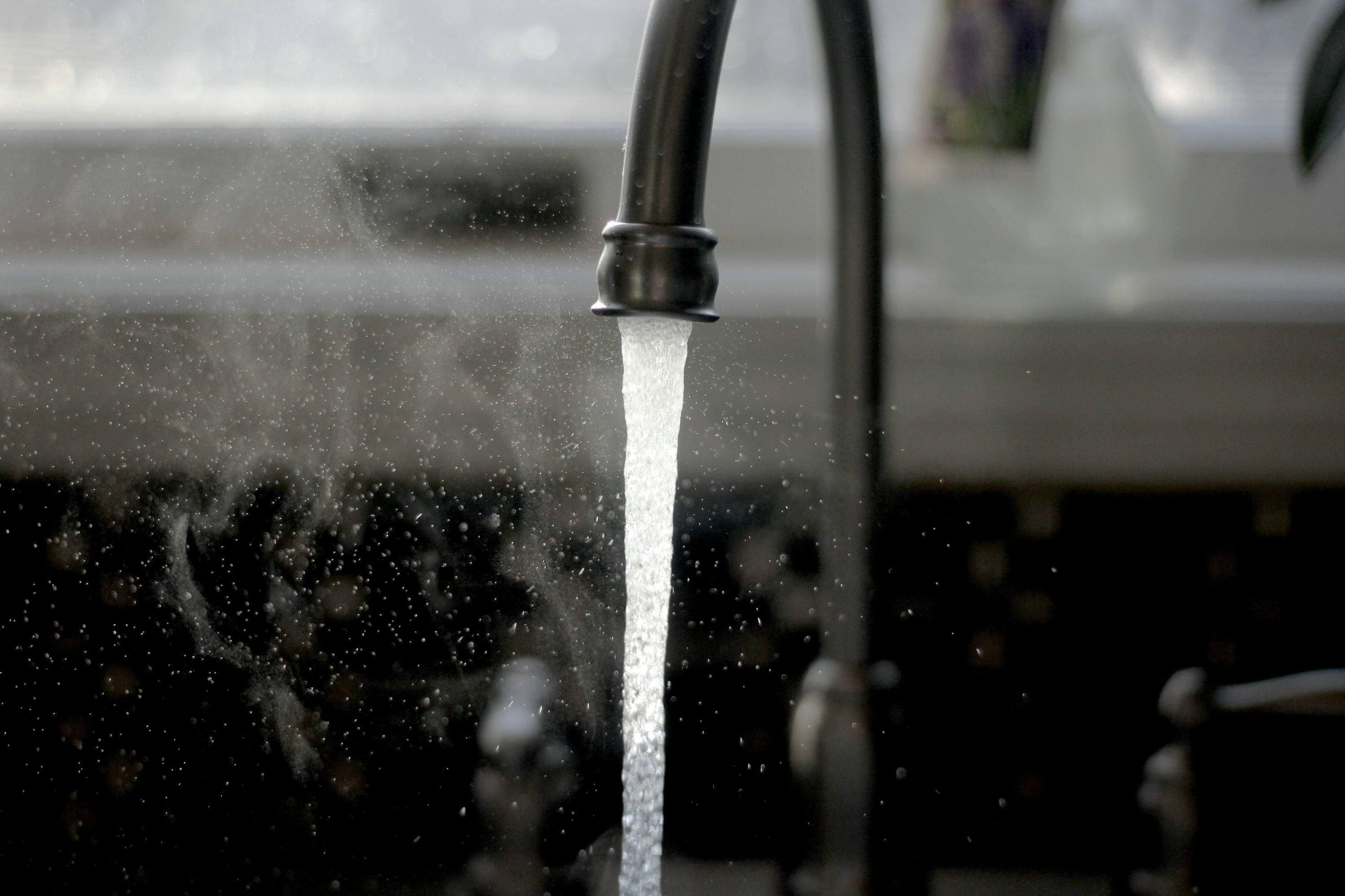 A faucet running cool water into a kitchen sink, used to gently cool a minor burn during first aid